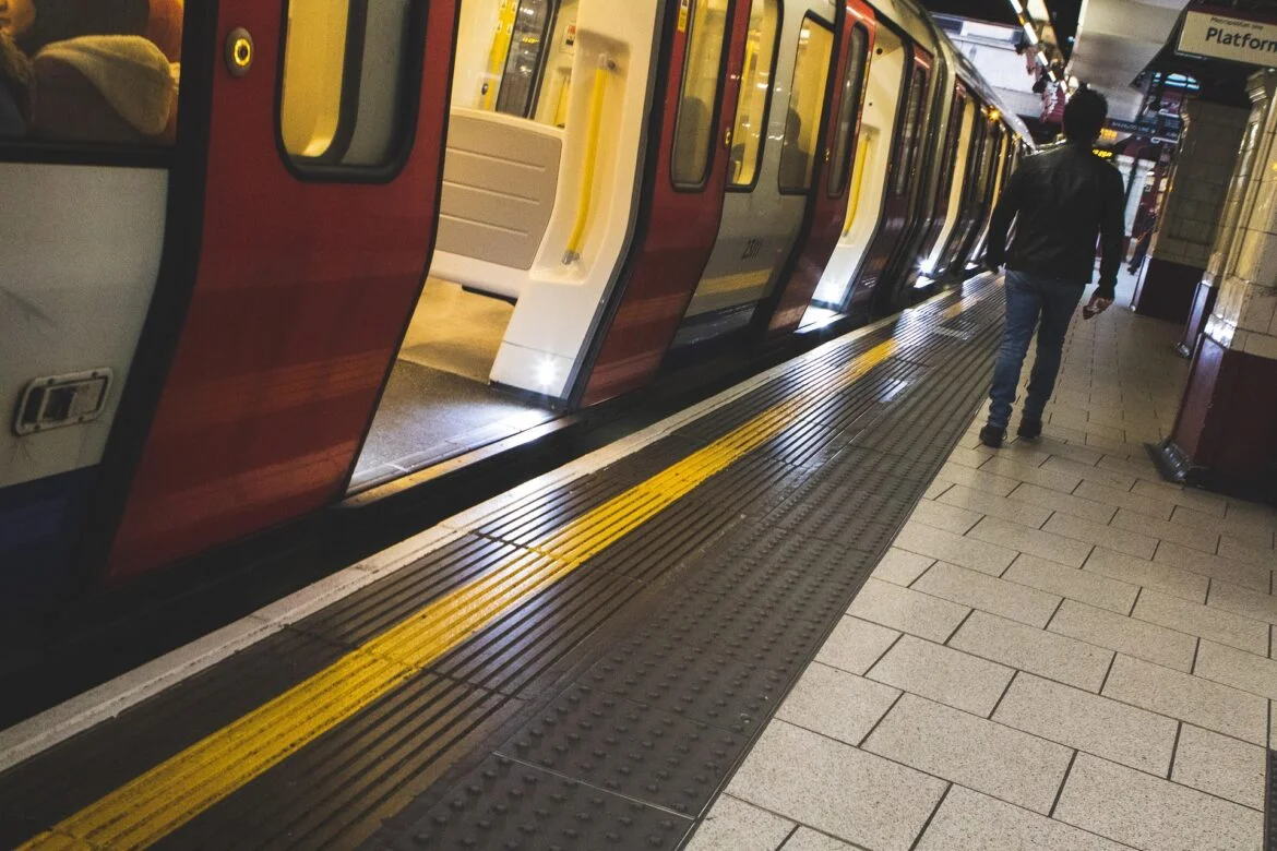 Subway platform with a red-and-gray train stopped at the platform; a man stands near the open doors.
