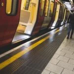Subway platform with a red-and-gray train stopped at the platform; a man stands near the open doors.