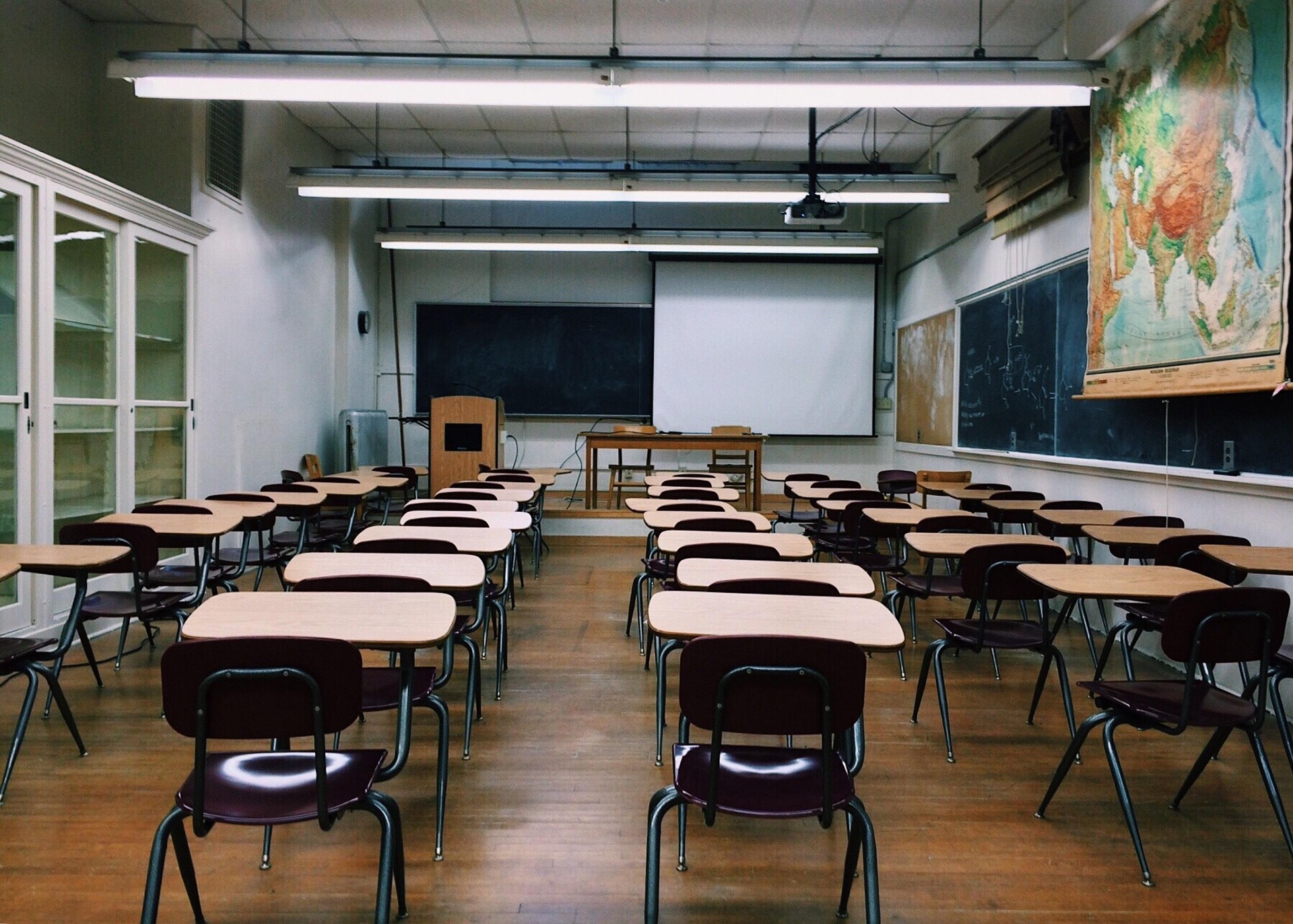 Empty classroom with rows of desks facing a chalkboard and projection screen at the front.