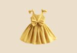Yellow polka-dot sleeveless dress for a girl with a large bow at the waist on a beige background.