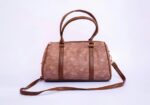 Brown leather handbag with two rounded handles and a long detachable strap against a pale background.