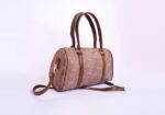 Brown cylindrical leather handbag with two handles and a detachable shoulder strap on a light background.