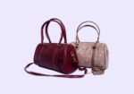 Two leather barrel handbags, burgundy and beige, with top handles and a detachable shoulder strap.
