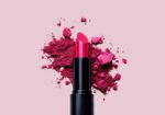 Bright pink lipstick in a black case with pink powder splashes on a pale pink background