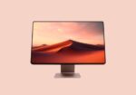 Wide computer monitor on a metal stand displaying a desert dunes wallpaper against a peach background, centered.