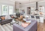 Bright open-plan living room and kitchen with a gray sofa, purple accent chairs, and a white kitchen island behind a breakfast bar.