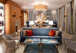 Upscale hotel lounge with a blue sofa, red pillows, cream chairs, glass coffee tables, and a large floral centerpiece.