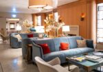 Luxurious hotel lounge with blue velvet sofas, red cushions, glass coffee tables, and warm ambient lighting.