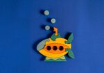 Colorful wooden pumpkin puzzle with green leaves on a blue background, featuring three black holes.